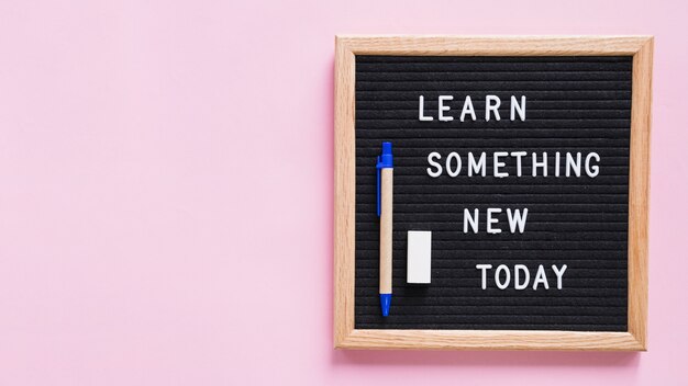 분홍색 배경 위에 펜과 지우개가있는 슬레이트에서 새로운 오늘의 텍스트를 배우십시오.