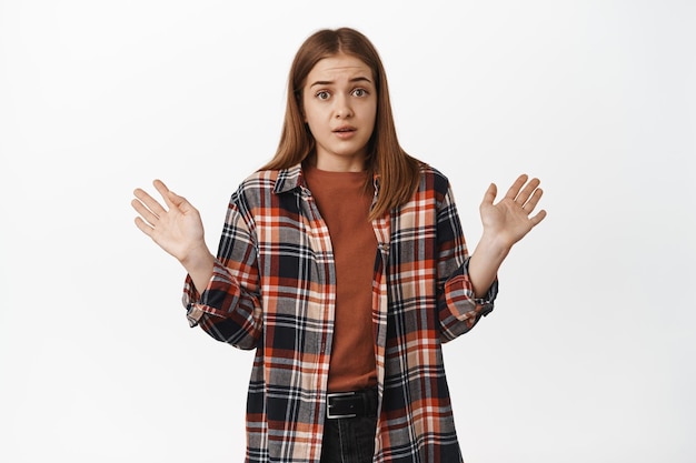 Leave me out of it. Reluctant girl looks alarmed, raising hands up in surrender, unwilling to participate in smth, refusing and rejecting offer, standing against white background