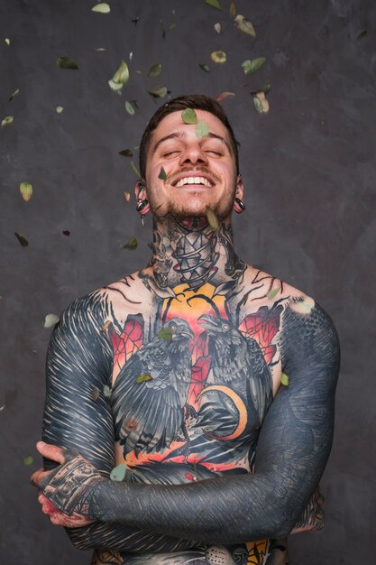 Leaves falling over the smiling tattooed young man with his arms crossed