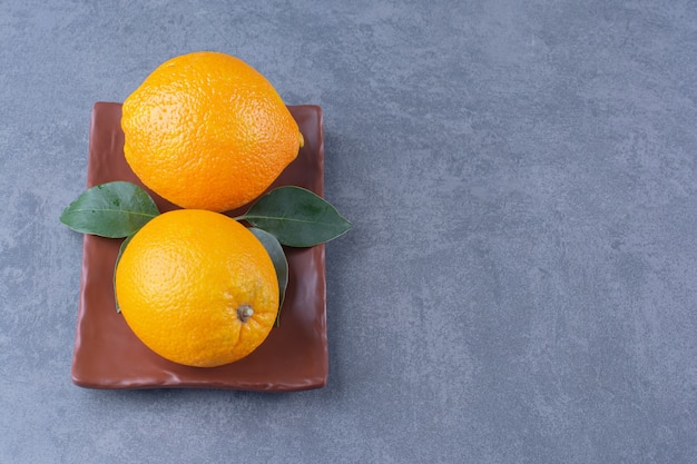Leaves and juicy oranges on wooden plate plate, on the dark surface