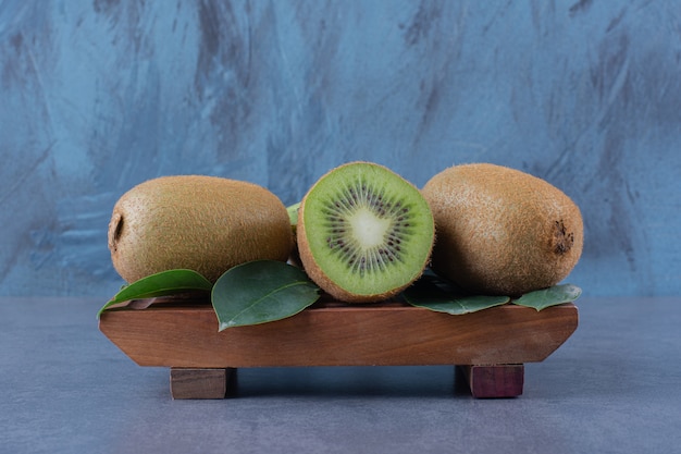 Leaves and kiwi on wooden plate on the dark surface