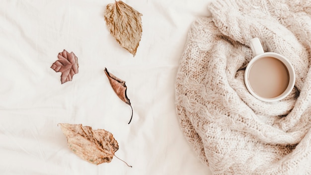 Leaves near hot drink in plaid on bedsheet