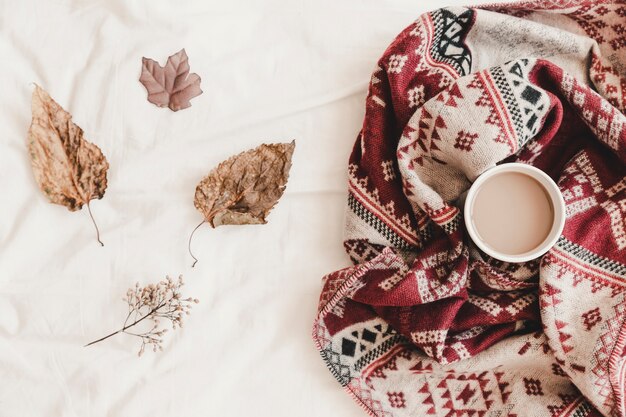 Leaves near hot drink in plaid on bedsheet 