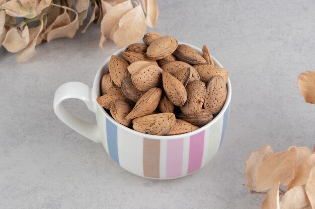 Leaves and a pile of almonds in the bucket on the marble surface