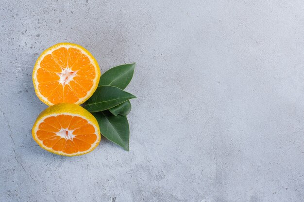 Leaves and tangerines slices bundled together on marble background. 