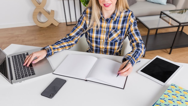 Леворукая женщина пишет в тетради на рабочем месте с ноутбуком