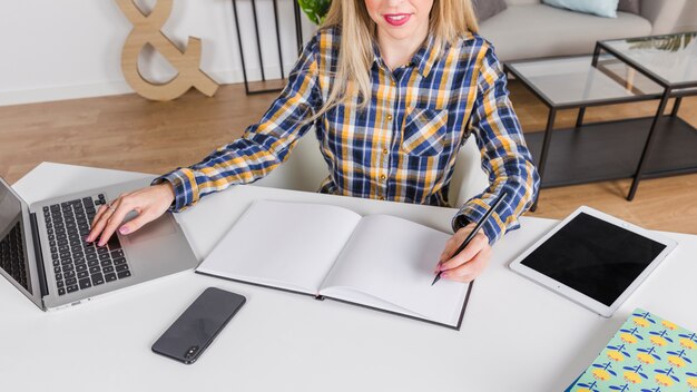 Left handed woman writing in notebook at workplace with laptop 