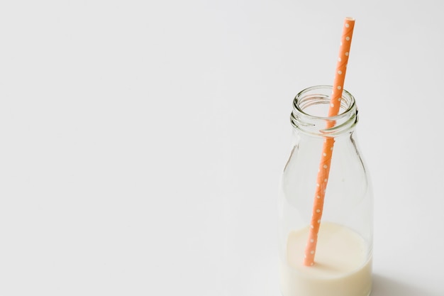 Leftover milk in the glass bottle with an orange straw on white background