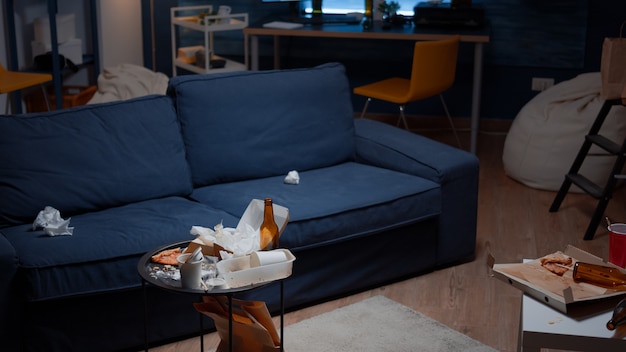 Leftover of pizza empty beer bottles and napkins on table in messy living room