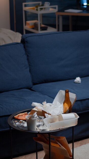 Leftover of pizza empty beer bottles and napkins on table in messy living room