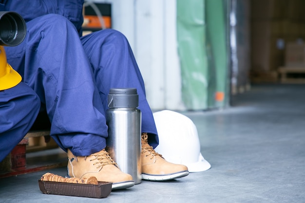 Legs of female plant worker sitting on floor near thermos and cookies