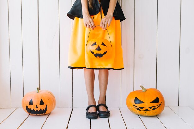 Legs of girl holding Halloween basket with pumpkins on sides 