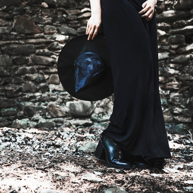 Legs of woman in black dress holding hat