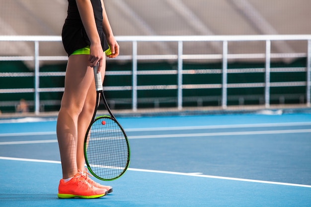 Legs of young girl in a closed tennis court with ball and racket