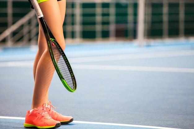 Legs of young girl in a closed tennis court with racket