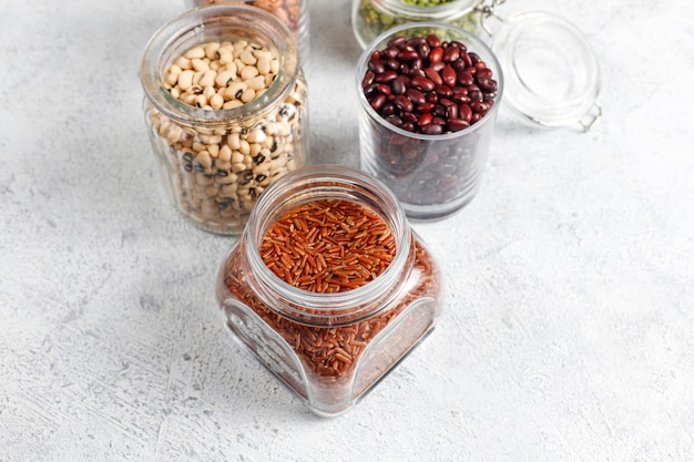 Legumes and beans assortment in different bowls on light stone background . Top view. Healthy vegan protein food.