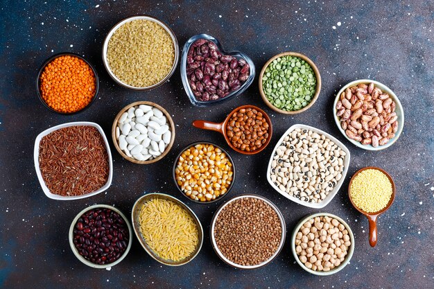 Legumes and beans assortment in different bowls on light stone background . Top view. Healthy vegan protein food.