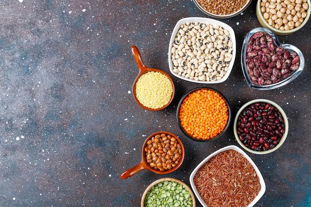 Legumes and beans assortment in different bowls on light stone background . Top view. Healthy vegan protein food.