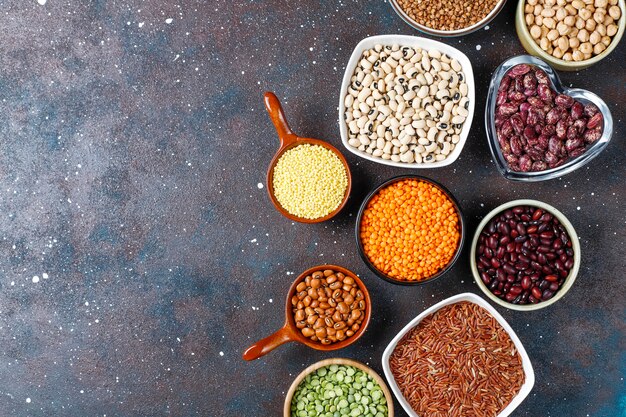 Legumes and beans assortment in different bowls on light stone background . Top view. Healthy vegan protein food.