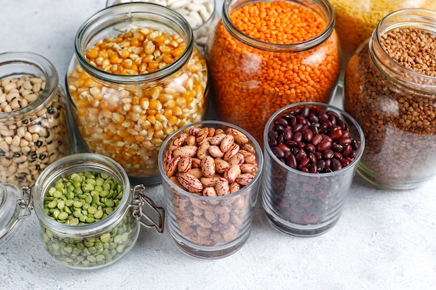 Foto gratuita assortimento di legumi e fagioli in diverse ciotole su fondo in pietra chiara. vista dall'alto. alimento proteico vegano sano.