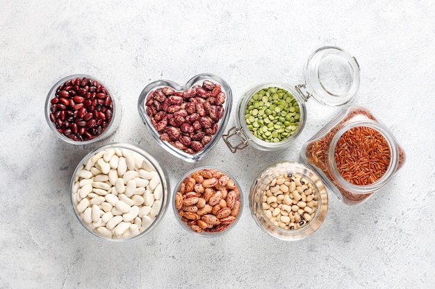 Legumes and beans assortment in different bowls on light stone background . Top view. Healthy vegan protein food.