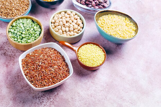 Legumes and beans assortment in different bowls on light stone background . Top view. Healthy vegan protein food.