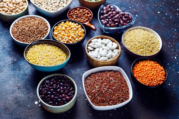 Legumes and beans assortment in different bowls on light stone background . Top view. Healthy vegan protein food.