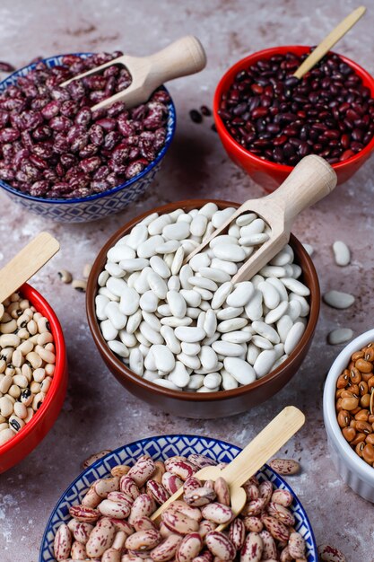 Legumes and beans assortment in different bowls on light stone background . Top view. Healthy vegan protein food.