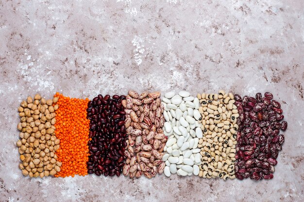 Legumes and beans assortment in different bowls on light stone background . Top view. Healthy vegan protein food.