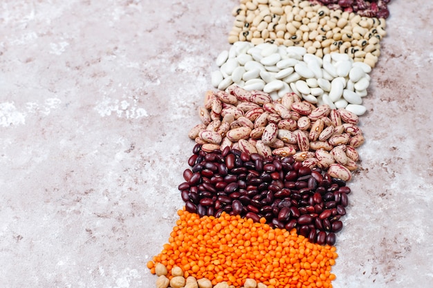 Legumes and beans assortment in different bowls on light stone background . Top view. Healthy vegan protein food.