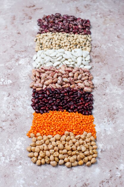 Legumes and beans assortment in different bowls on light stone background . Top view. Healthy vegan protein food.