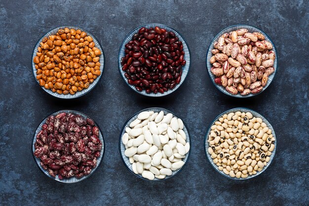 Legumes and beans assortment in different bowls on light stone surface . Top view. Healthy vegan protein food.