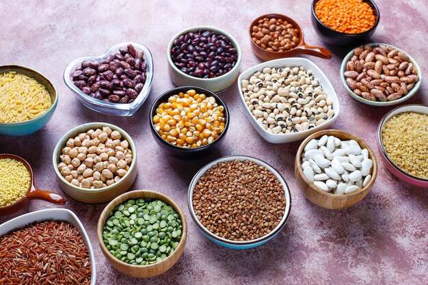 Legumes and beans assortment in different bowls on light stone table . Top view. Healthy vegan protein food.