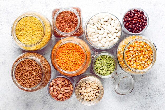 Legumes and beans assortment in different bowls on light stone . Top view. Healthy vegan protein food.