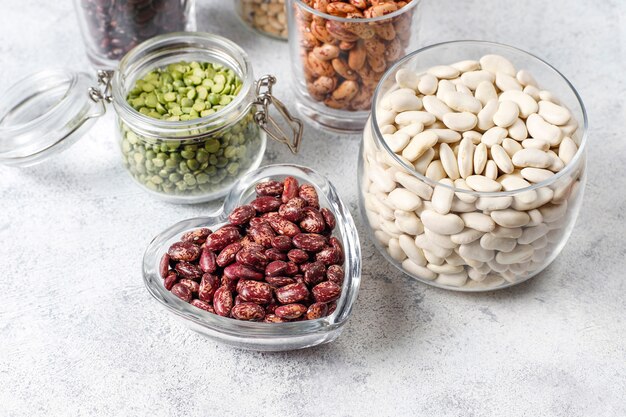 Legumes and beans assortment in different bowls on light stone