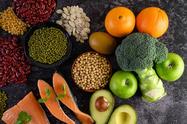 Legumes, broccoli, fruit, and salmon placed on a black cement floor.