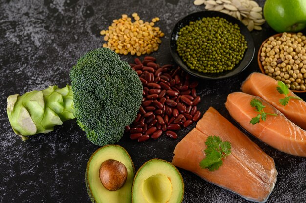 Legumes, broccoli, fruit, and salmon placed on a black cement floor.