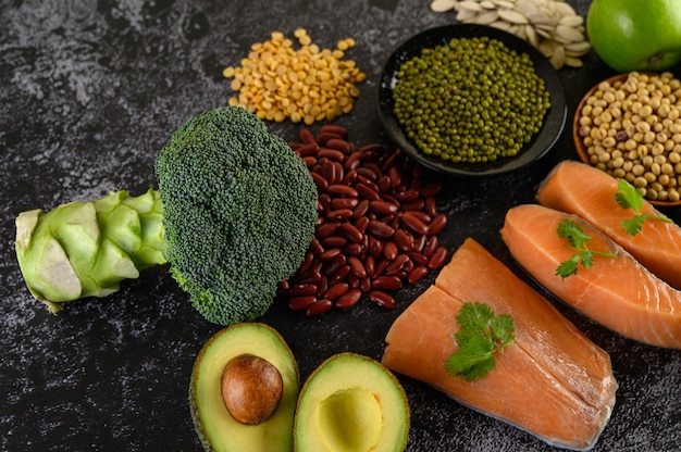 Legumes, broccoli, fruit, and salmon placed on a black cement floor.