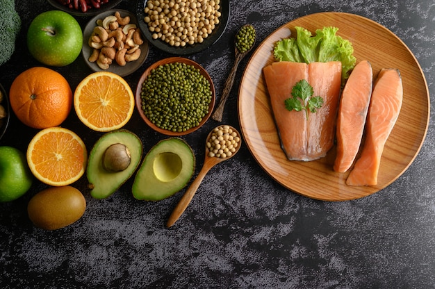 Legumes, fruit and salmon pieces on a wooden plate.