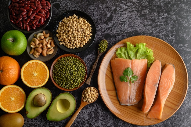 Legumes, fruit and salmon pieces on a wooden plate.