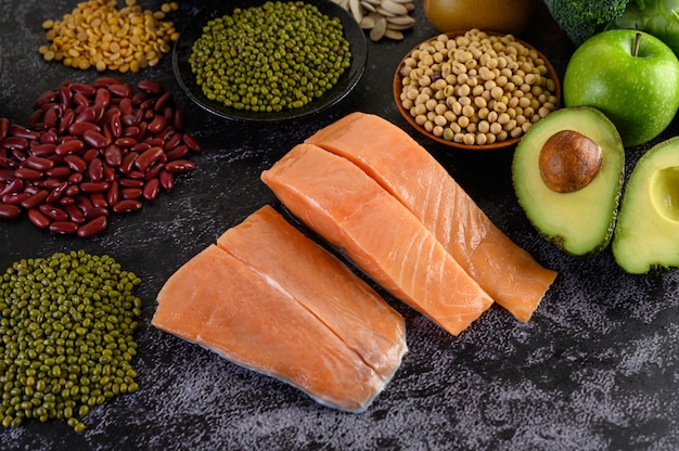 Legumes, fruit, and salmon placed on a black cement floor.