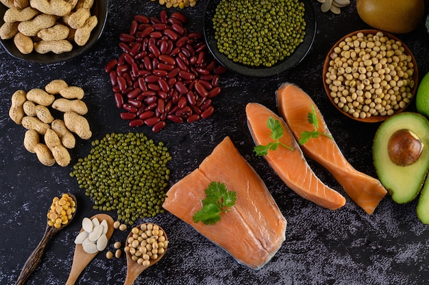 Legumes, fruit, and salmon placed on a black cement floor.