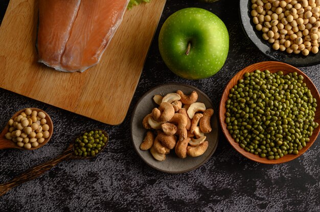 Legumes, salmon pieces and apple on a black cement floor surface.