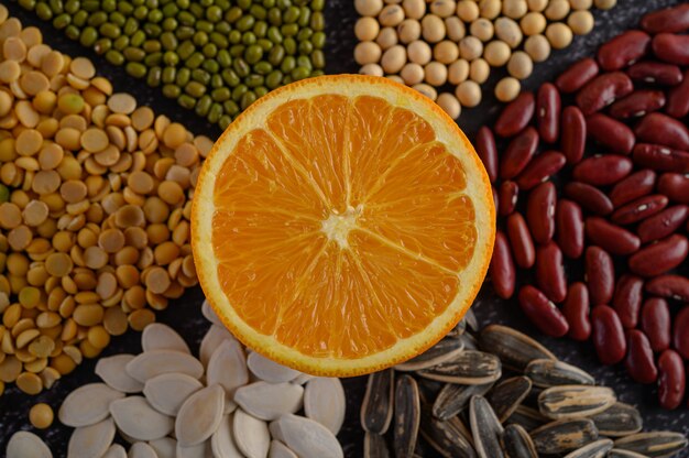 Legumes with Orange cut in half on a black cement floor surface.