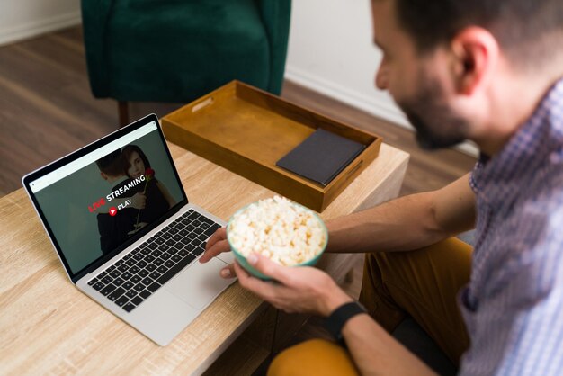 Leisure day. Happy man searching for a fun movie on an online streaming service while eating popcorn