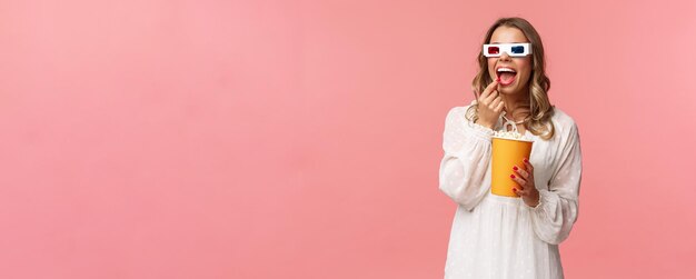 Leisure goingout and spring concept Portrait of attractive young woman in white dress enjoying watching interesting movie on full screen at cinema eating popcorn and wearing 3d glasses