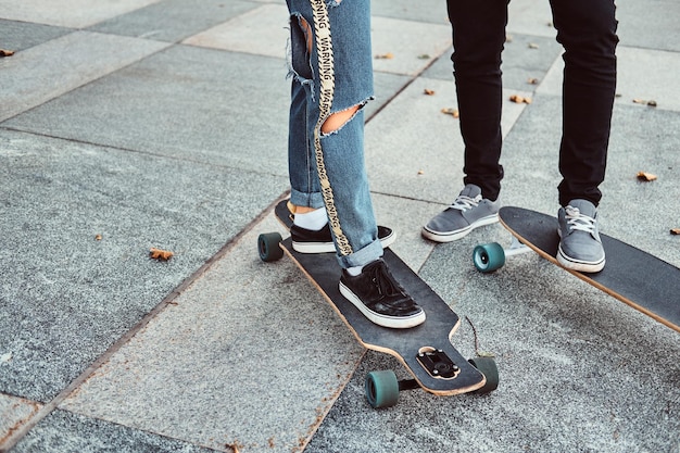 Leisure and sport concept - close-up photo of a trendy dressed teen couple with skateboards on the street.