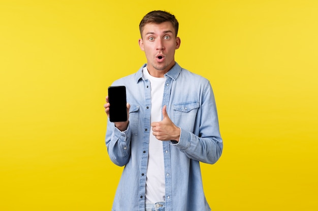 Leisure, technology and application advertisement concept. Excited and surprised handsome man showing thumbs-up as describe amazing mobile phone app, showing smartphone screen.