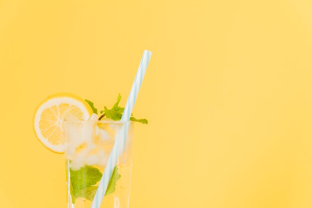 Lemon cocktail with plastic straw on yellow background