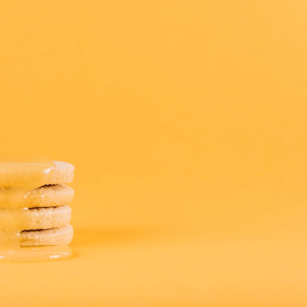 Lemon curd dripping over stack of fresh cookies on yellow surface